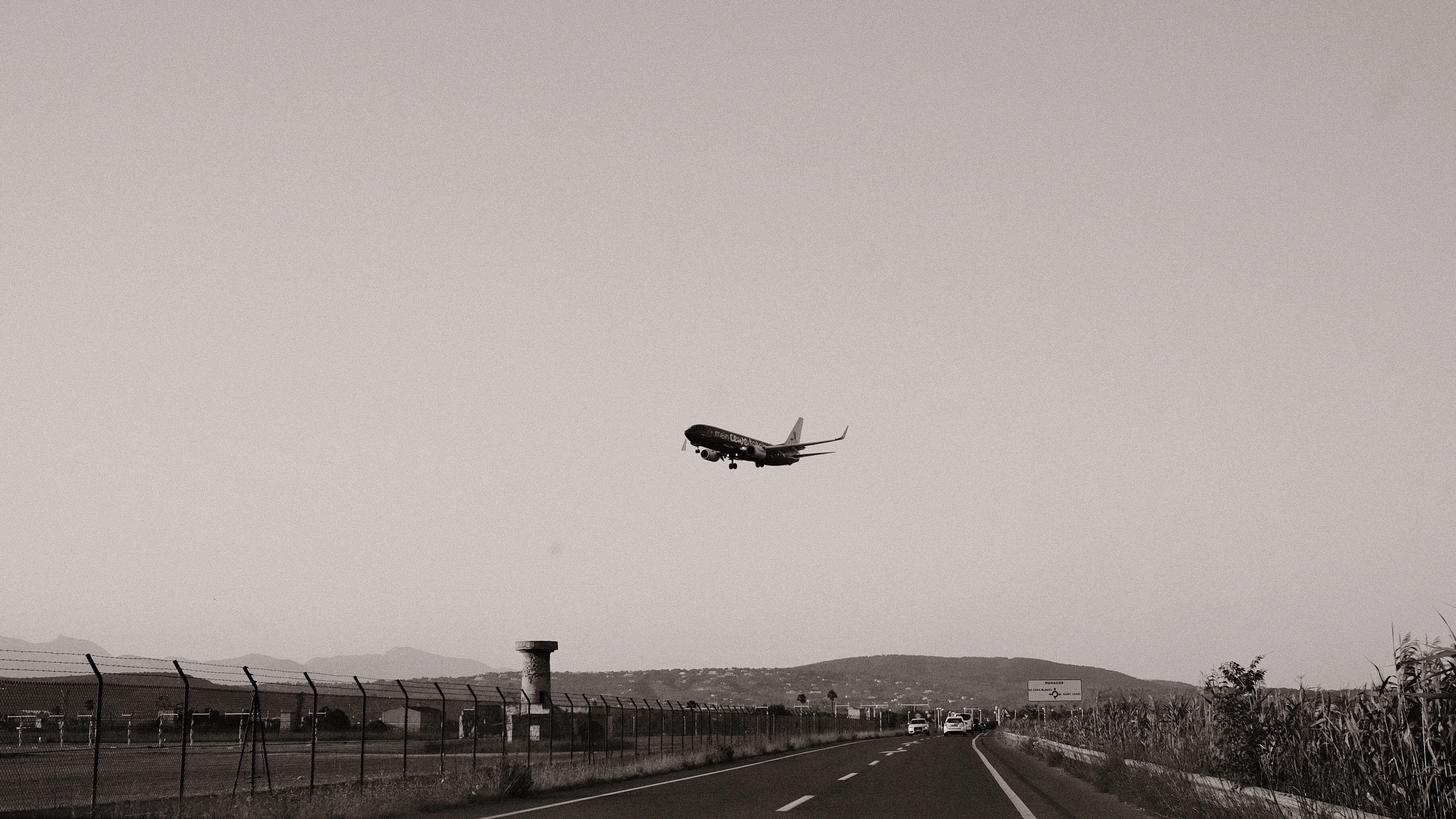 Airplane approaching palma de mallorca airport over coastal road black and white