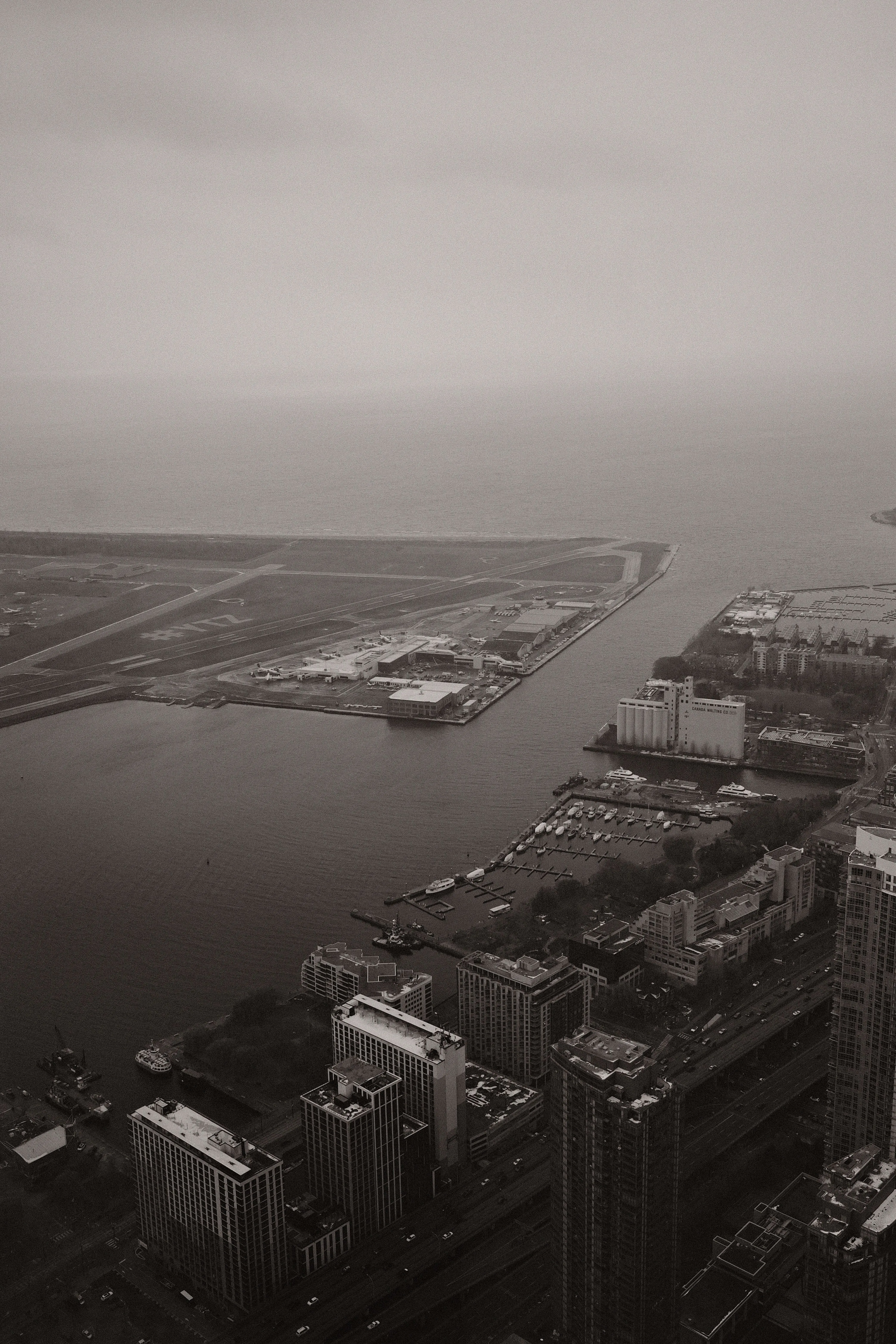 Black and white aerial view of city waterfront airport runway and harbor on overcast day
