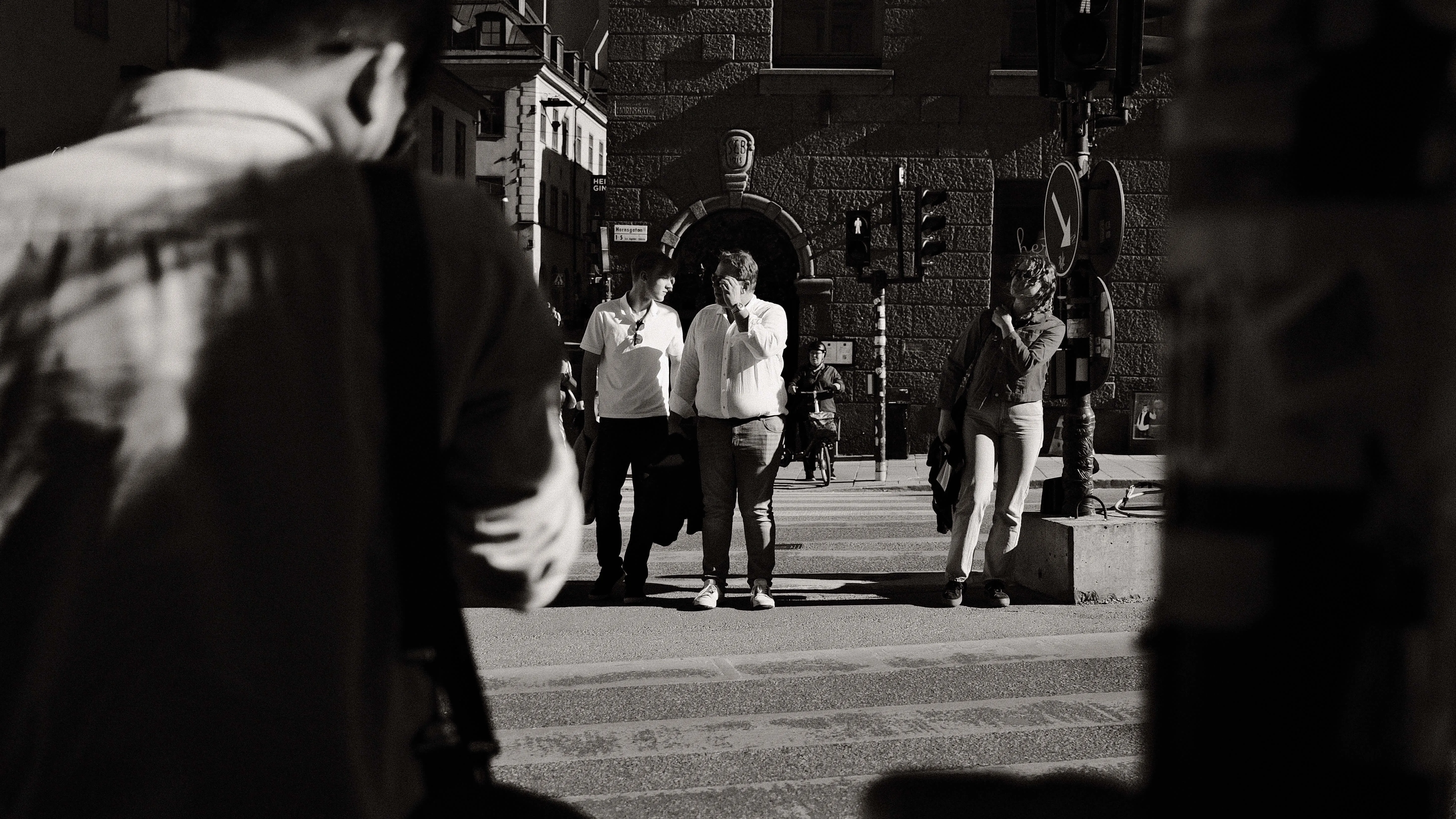 People waiting at crosswalk framed by foreground figures stockholm black and white