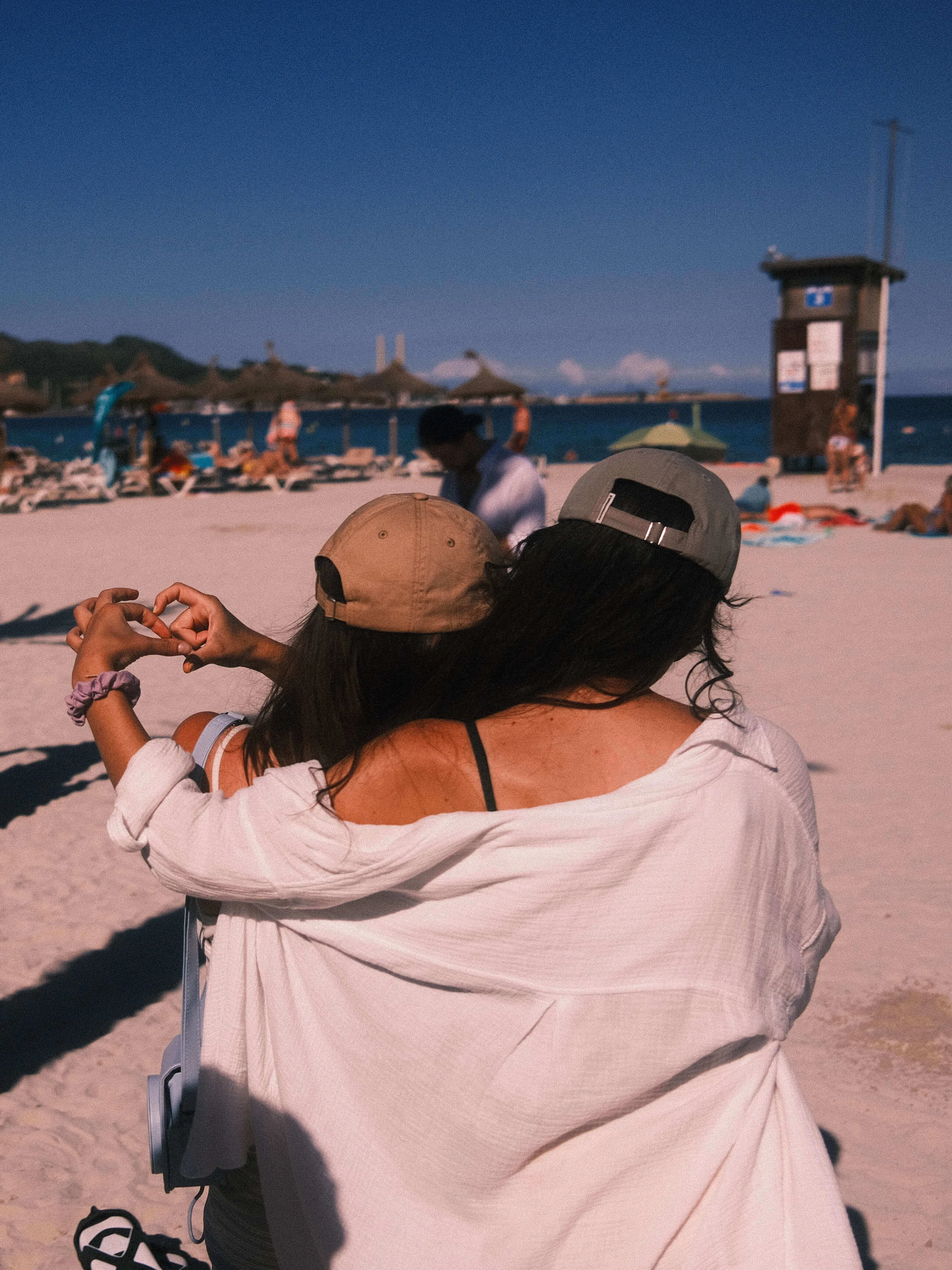 Two women sitting on beach forming heart with hands