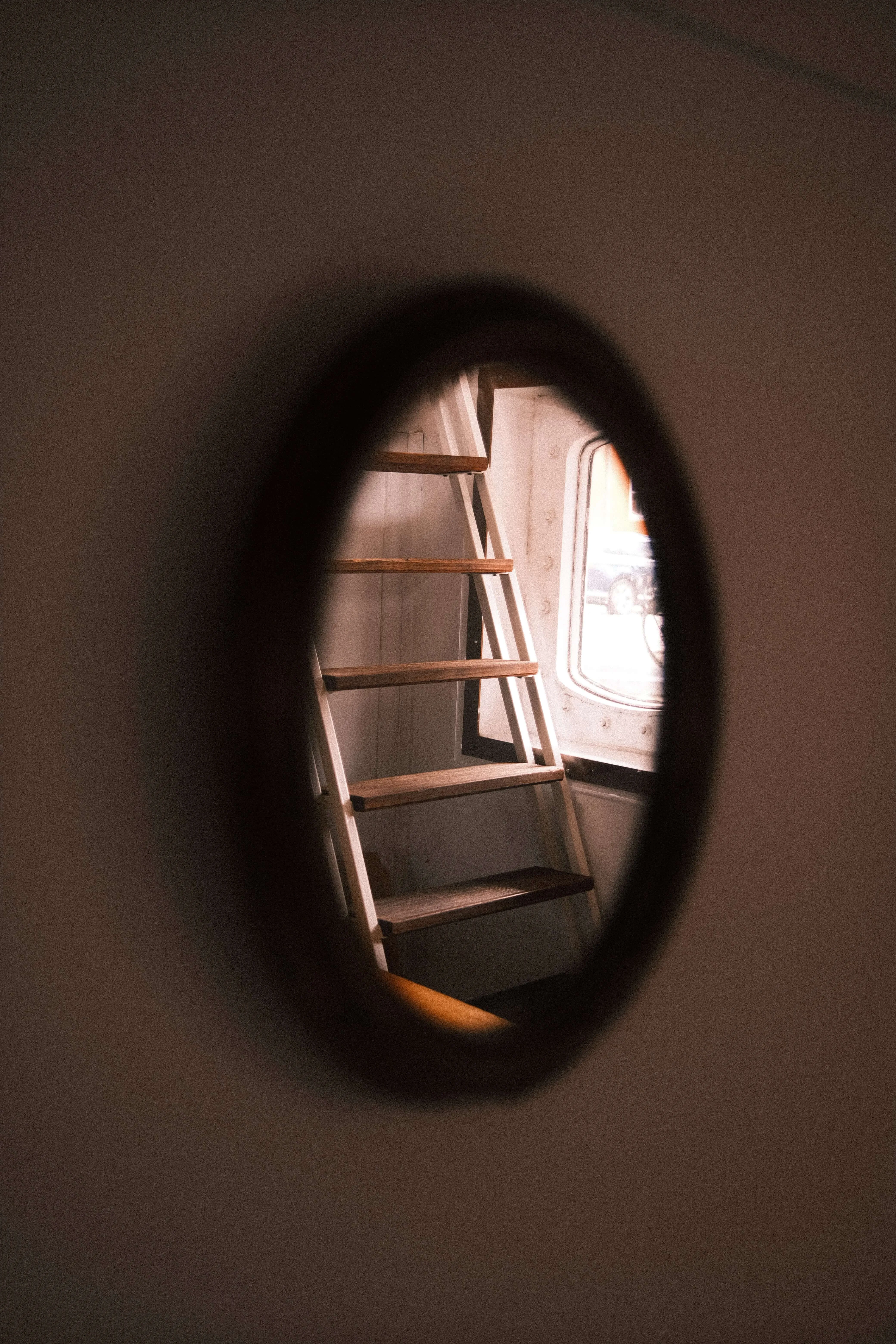 Ladder and window seen through round opening inside boat or ship cabin
